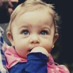 A baby looks up above the camera with its finger in its mouth