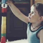 A young boy plays with wooden building blocks, building a tower
